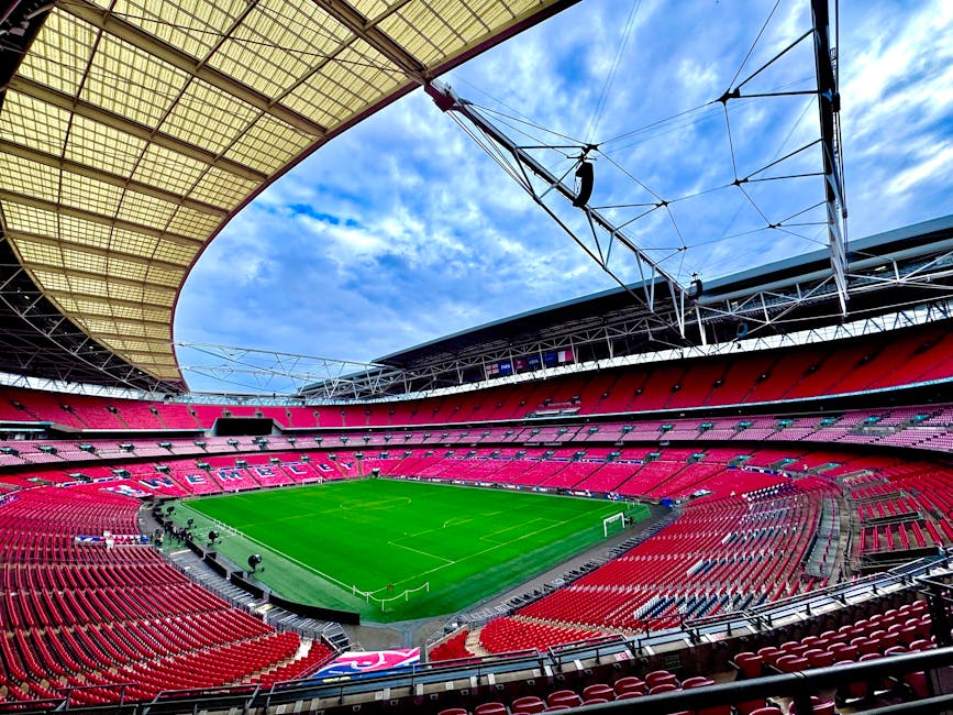 Inside Wembley Stadium during daytime, the image showcases a large football pitch with lush green grass, clearly marked with white boundary lines and goal areas. In the foreground, there are a few ind